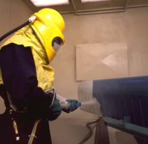 Someone sand blasting an industrial part
